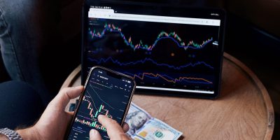 Two people using smartphone and tablet for trading stocks indoors.