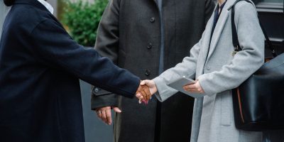 Crop anonymous diverse businesswomen in trendy elegant coats shaking hands after important conference on street