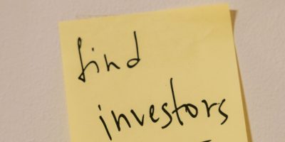 Close-up of a handwritten note reminding to find investors, on a wall.